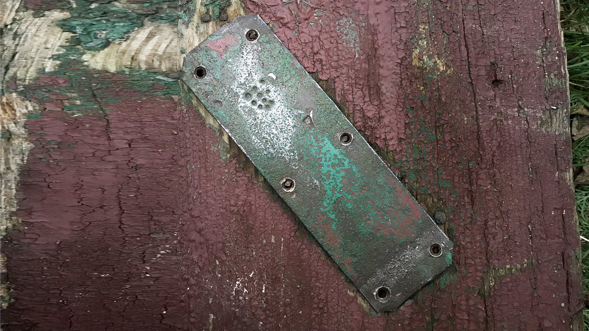 Old metal mezuzah plate with letter Shin on a weathered doorframe, showing pre-war primitive construction and mezuzah trace