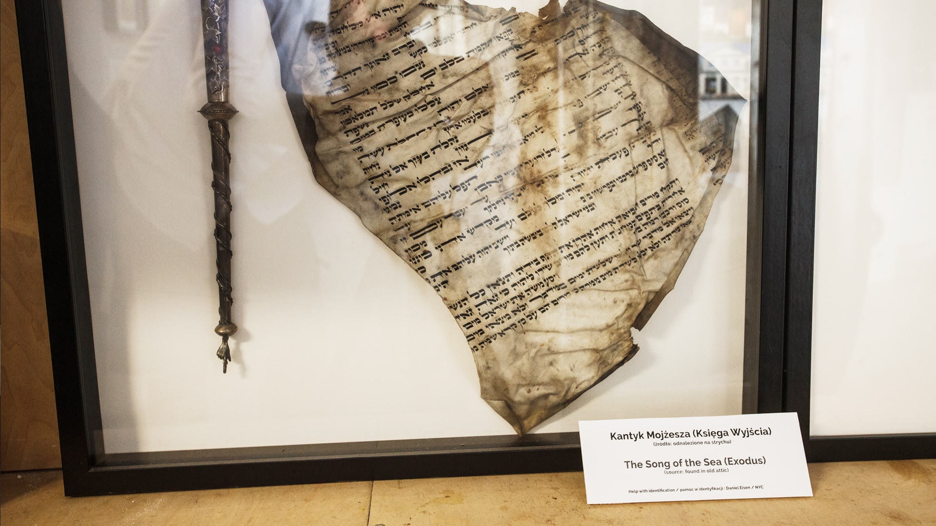 Display case with a silver Torah pointer and a burnt Hebrew manuscript titled “The Song of the Sea (Exodus)”