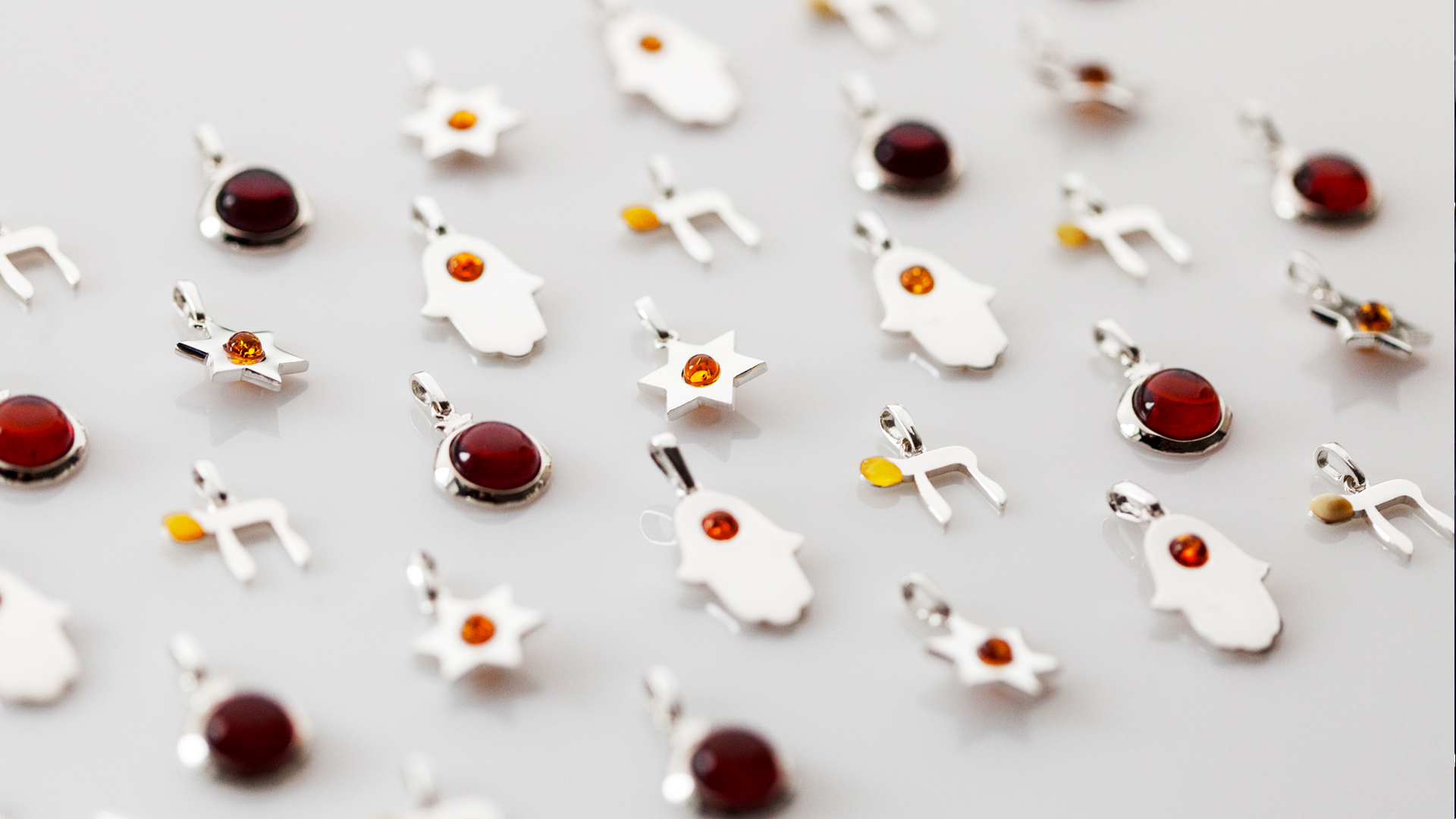 Small double-sided silver and amber pendants featuring Jewish motifs like stars, hamsas, and Hebrew letters, drawing inspiration from mezuzah trace, designed by MI POLIN design